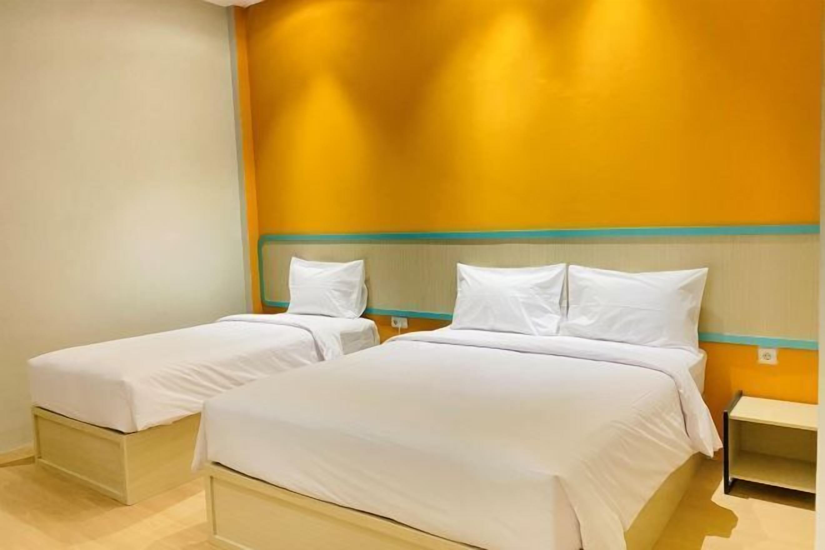 A hotel room with two single beds, a small bedside table, and a wall with a yellow accent.