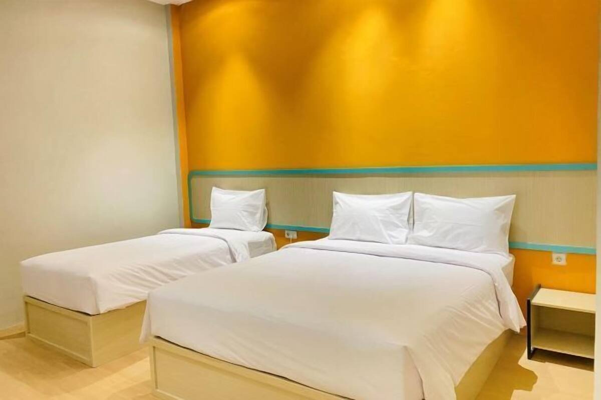 Une chambre d’hôtel avec deux lits simples, une petite table de chevet et un mur avec une touche de couleur jaune.