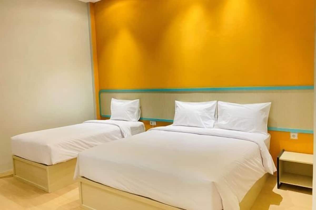 A hotel room with two single beds, a small bedside table, and a wall with a yellow accent.