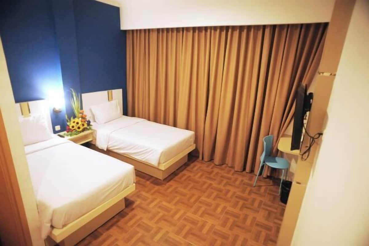 Une chambre d’hôtel avec deux lits, un parquet en bois, un bureau avec une chaise et un téléviseur.