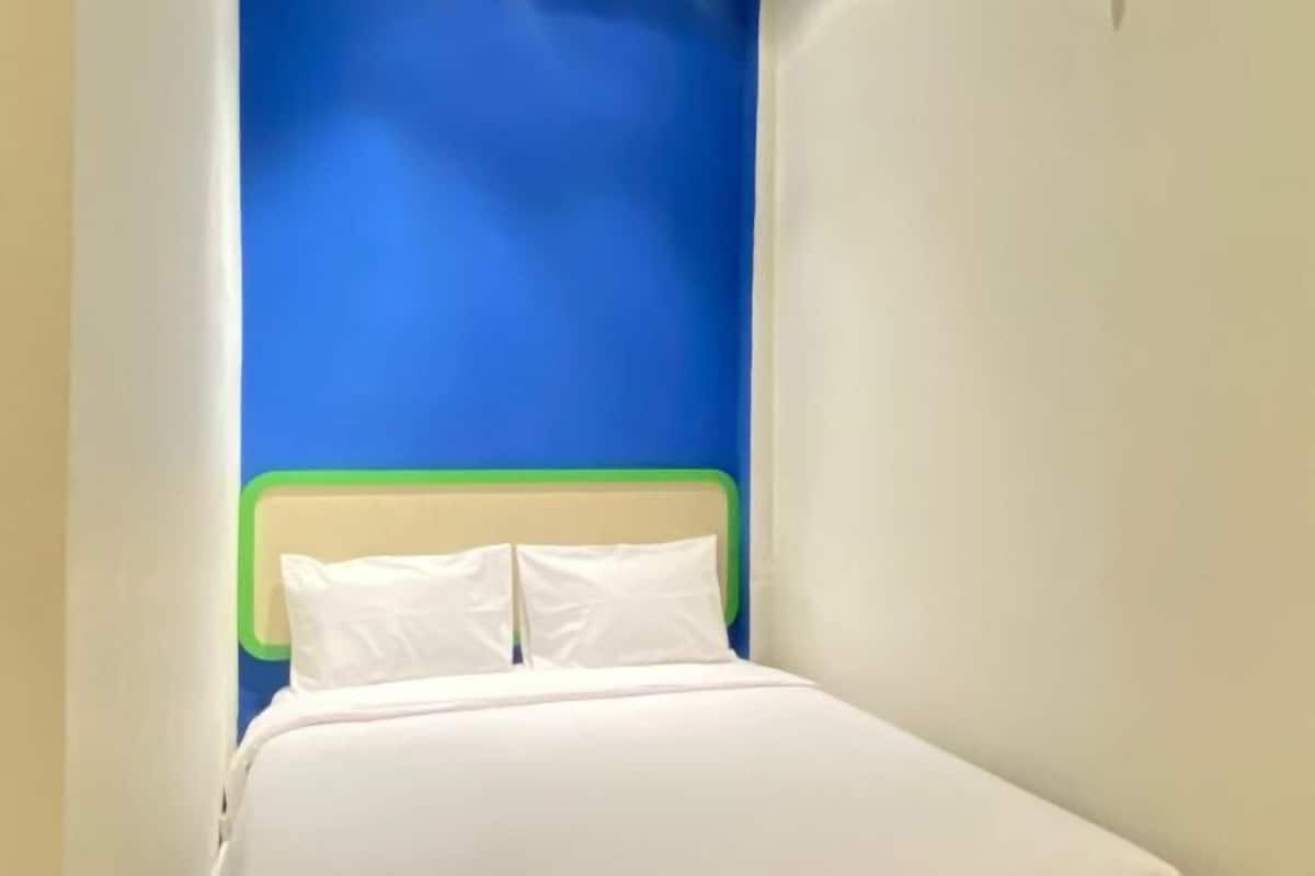 Une petite pièce étroite avec un lit adossé à un mur bleu.