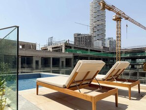 Uma área de piscina no terraço com espreguiçadeiras, vista para um canteiro de obras e um edifício alto em construção.