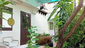 A courtyard with a white building, a door, a window with a target on the wall, a table with chairs, and potted plants.