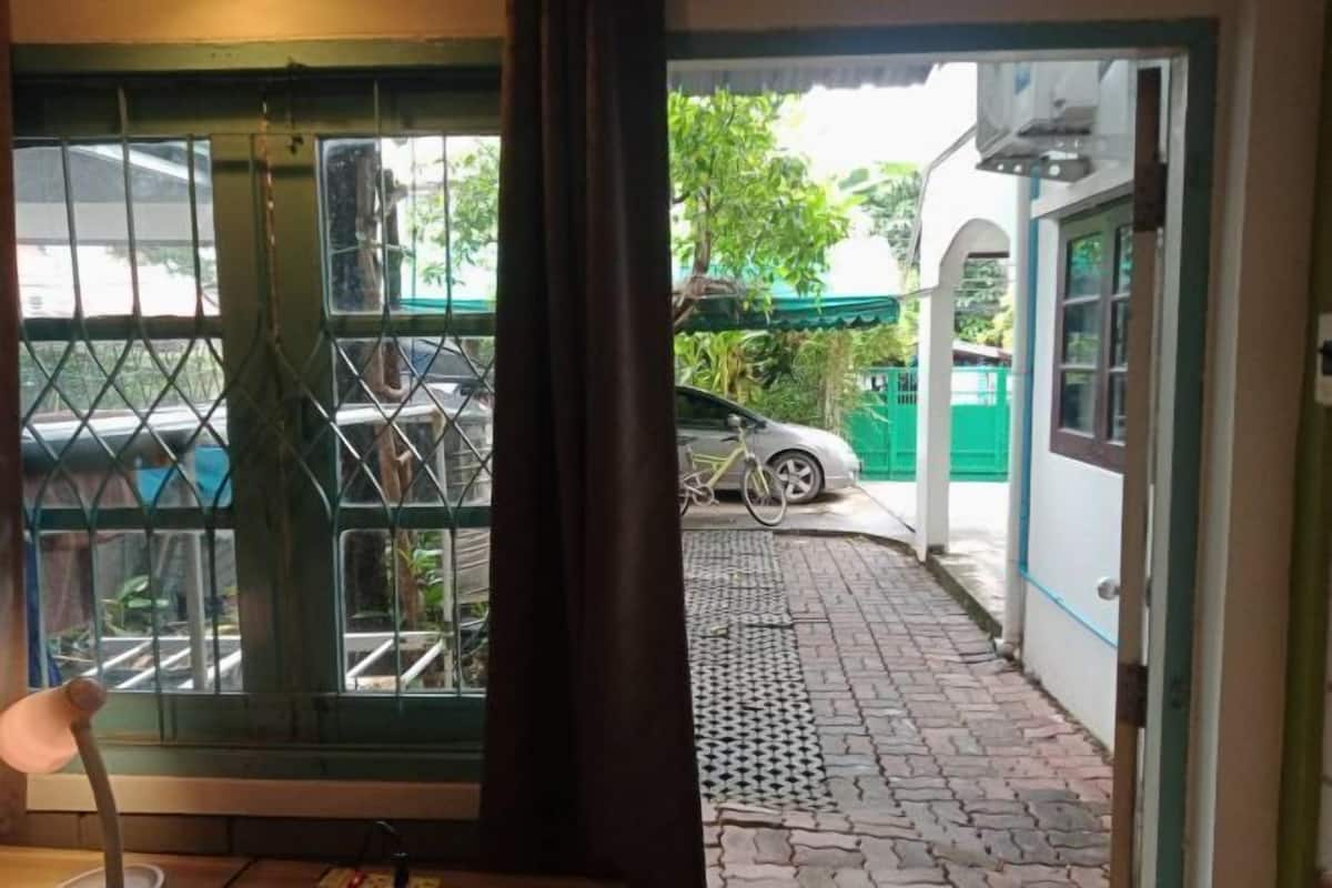 A view through a window with a metal gate, a bicycle, and a paved path leading outside.