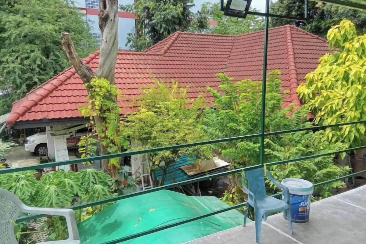 A residential area with a red-tiled roof house, green foliage, and a blue bucket on a balcony.