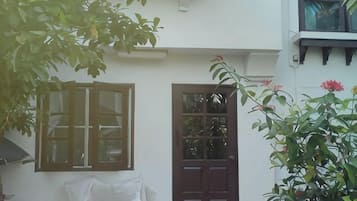 Edifício branco com porta marrom, janela emoldurada em madeira e área coberta com tecido branco.