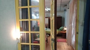 A room with a bed, a desk, and a chair. There is a window with curtains, and a door leading to another room.