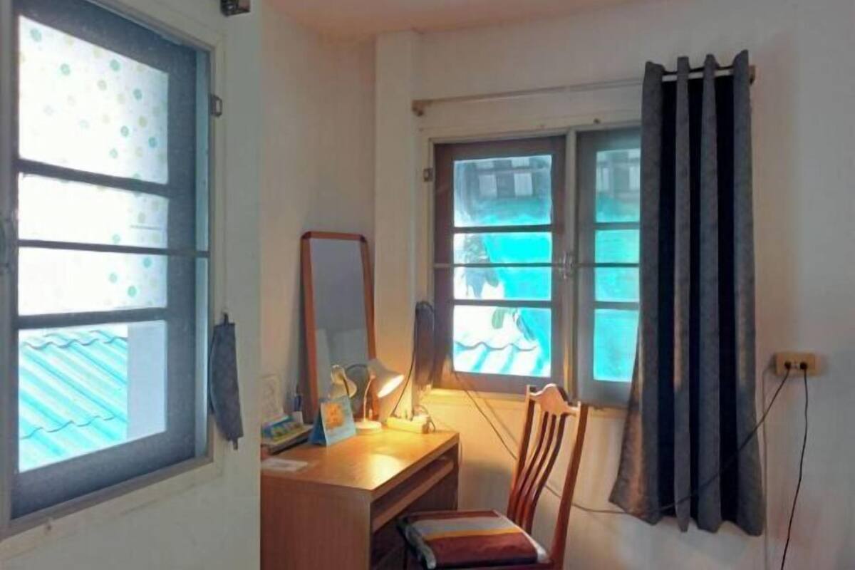 A room with a desk, chair, and two windows with curtains.