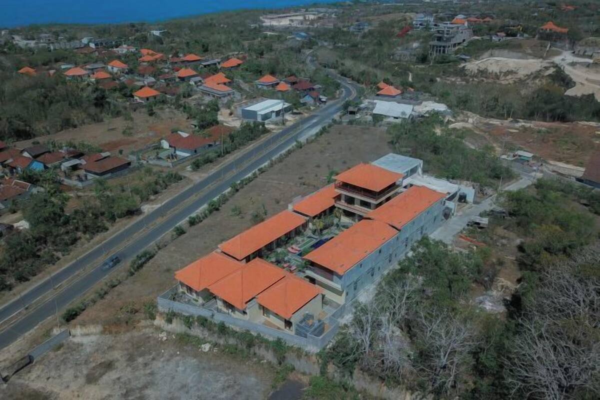 An aerial view of a residential area with houses having red roofs, a main road, and a large building with a blue facade.