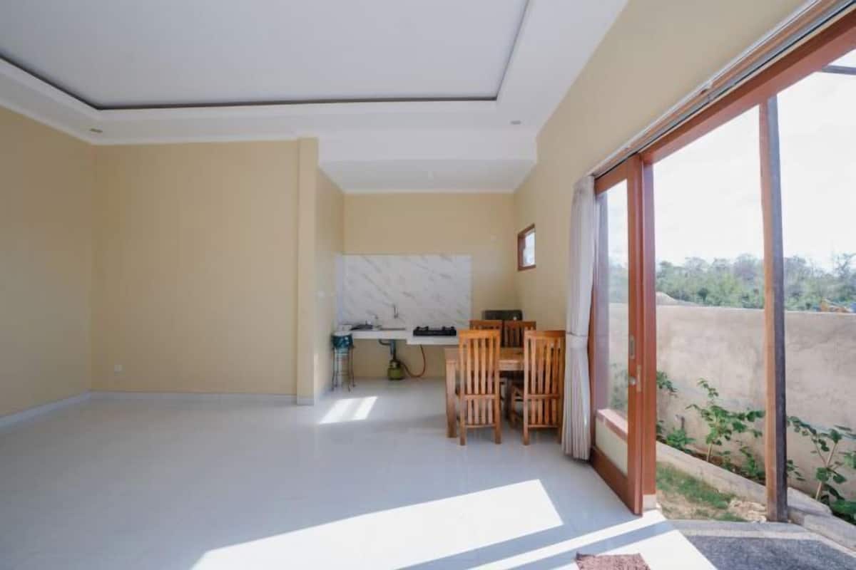 A spacious room with a large sliding glass door leading to a balcony, a kitchen area with a marble backsplash, and a dining table with chairs.