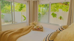 Un dormitorio con cama, una bandeja con objetos y vistas al verdor exterior.