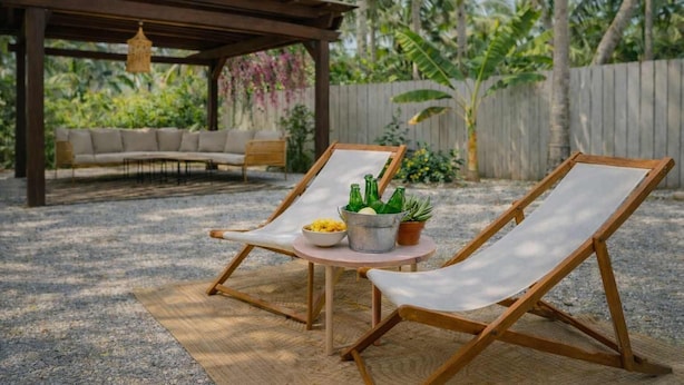 Dos sillones de madera con cojines, una mesita redonda con un frutero y botellas, y un farol colgante.