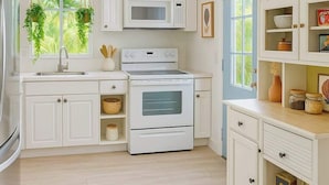 Una cocina moderna con armarios blancos, un microondas, un horno y una lámpara colgante.