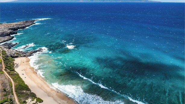 Un paisaje costero con aguas azules cristalinas, una playa arenosa y montañas al fondo.