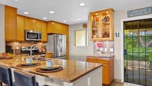 A modern kitchen with wooden cabinets, stainless steel appliances, and a granite countertop. - Ocean views, 2BR retreat, Less than 5 Minutesʻ to the Beach - Kaanapali Plantation 20 (Lahaina)