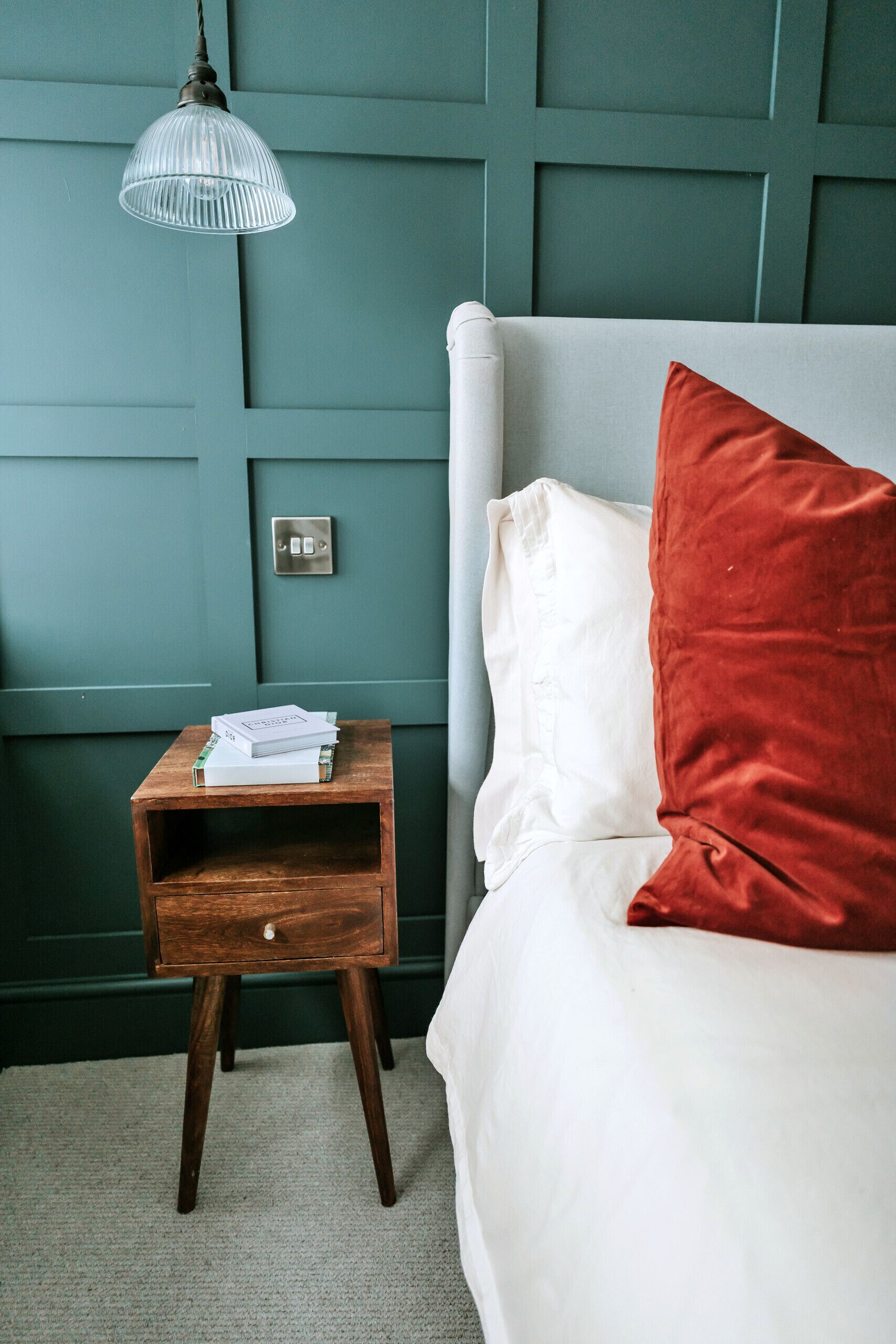 A bedroom with a bed, a nightstand, a lamp, and a wall switch.