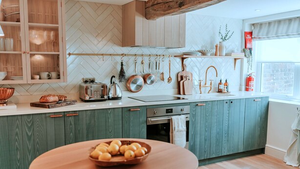 Eine moderne Küche mit Holzausbau, einer Fischgrätmuster-Fliesenrückwand und einem Holztisch mit Obstschale.