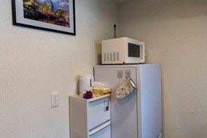 A small kitchenette with a microwave on top of a refrigerator, a power outlet on the wall, and a framed picture above the microwave. - Bainan Service Apartment (Osaka)