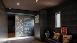 A modern interior with a dark-toned reception area, a bench with cushions, and a wall with multilingual welcome message. - Bainan Service Apartment (Osaka)