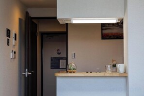 Une chambre d’hôtel avec un comptoir de réception, une porte, un luminaire fixé au mur et une petite étagère sur laquelle se trouve un objet décoratif.