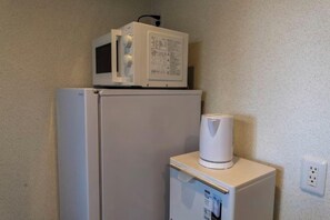 A small kitchenette with a microwave on top of a refrigerator and a coffee maker on a small table. - Bainan Service Apartment (Osaka)