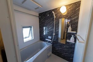 A bathroom with a bathtub, a shower, and a marble wall. - Bainan Service Apartment (Osaka)
