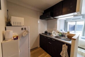 A compact kitchen with a refrigerator, microwave, and a small countertop. - Bainan Service Apartment (Osaka)