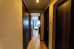 A narrow hallway with wooden flooring and dark doors, leading to a room with a bed and a window. - Bainan Service Apartment (Osaka)