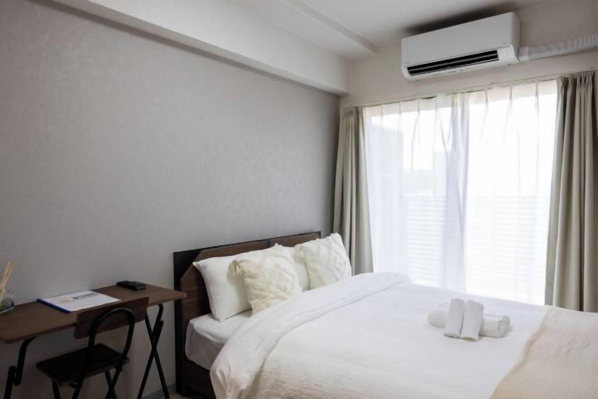 A hotel room with a bed, a desk, and an air conditioning unit.