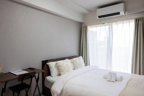 A hotel room with a bed, a desk, and an air conditioning unit. - Bainan Service Apartment (Osaka)