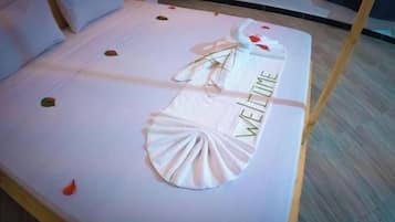 Un lit avec une serviette blanche pliée et un objet décoratif sur lequel est écrit le mot « BIENVENUE ».