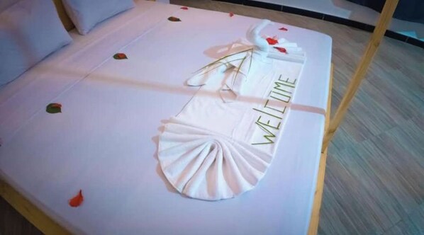 A bed with a folded white towel and a decorative item with 'WELCOME' written on it.