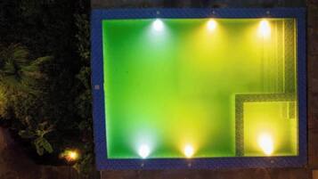 Une piscine rectangulaire bordée de bleu, avec quatre lampes placées aux coins.
