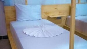 Un lit simple avec un cadre en bois et un baldaquin, une literie blanche et une serviette blanche soigneusement pliée posée sur le lit.