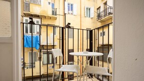A small balcony with a white table and two chairs, surrounded by a black metal fence.