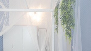 A room with a bed, a white wardrobe, and a hanging plant.