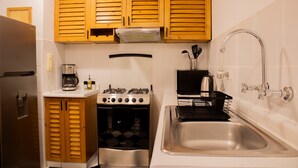 A compact kitchen with wooden cabinets, a stainless steel refrigerator, a gas stove, an oven, and a sink with a faucet. - w Stylish Bright 2BR in Miraflores (Lima)