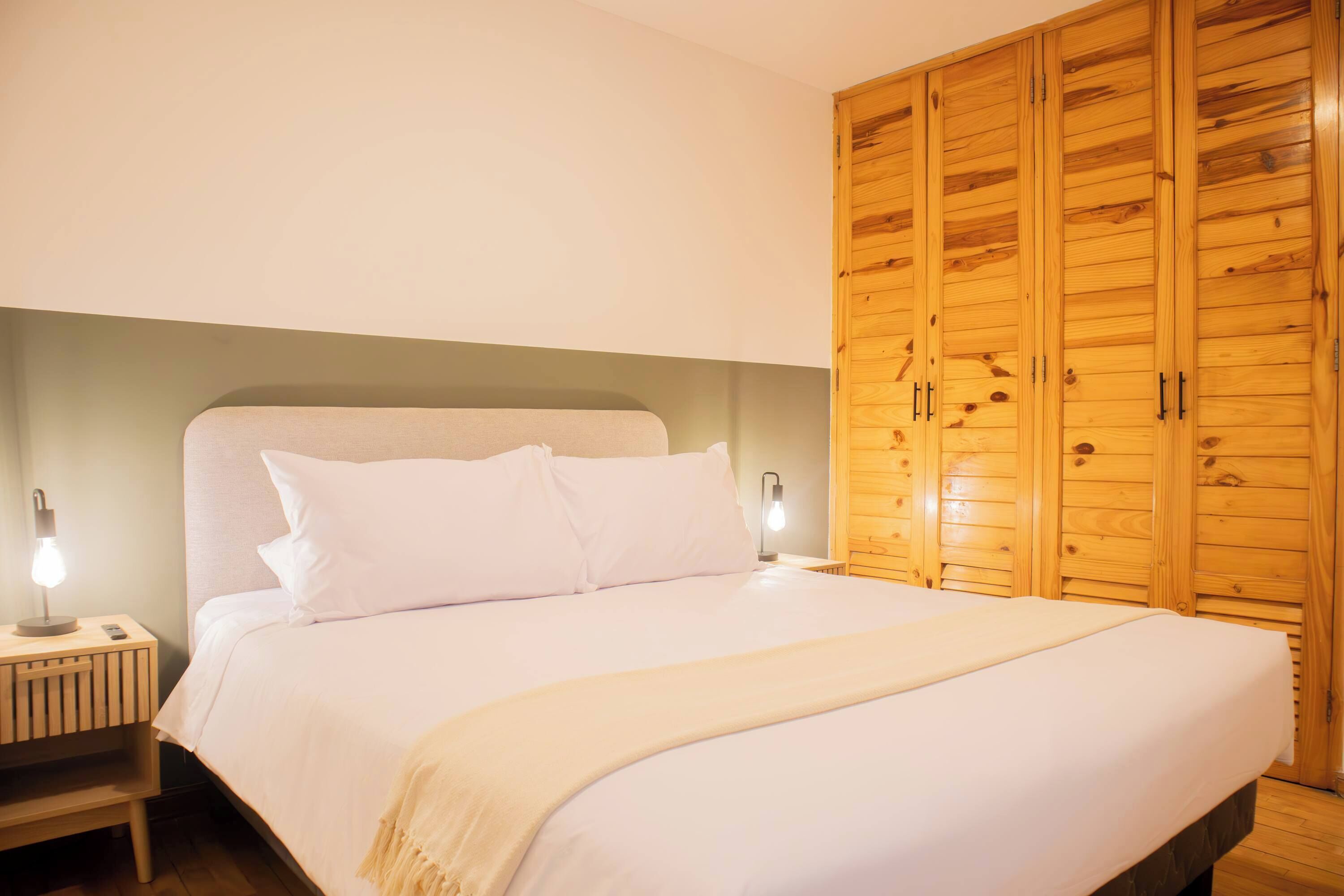 Une chambre à coucher avec une armoire en bois, une table de chevet avec une lampe et un lit avec une literie blanche.