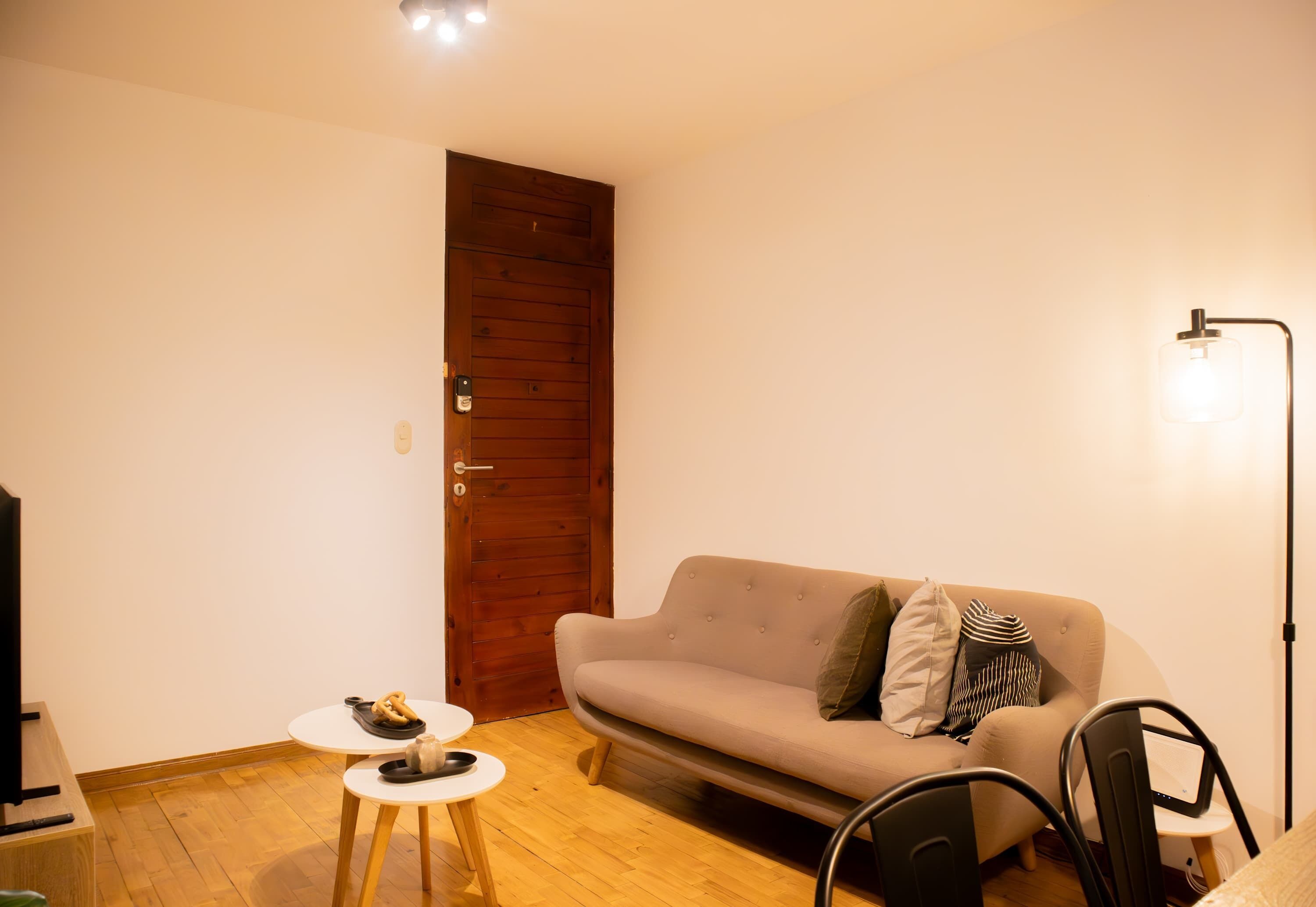 A living room with a wooden door, a beige sofa, a small round table, and a black chair.