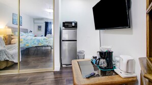 Ein Hotelzimmer mit einem Bett, einem Schreibtisch mit einem Laptop, einer Kaffeemaschine und einem an der Wand montierten Fernseher.