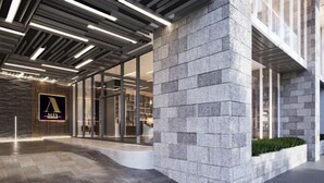 Un hall d’hôtel moderne avec une façade en pierre, une entrée en verre et un intérieur bien éclairé.