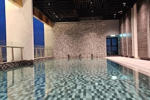 An indoor swimming pool with a checkered floor, stone wall, and a view of the city.