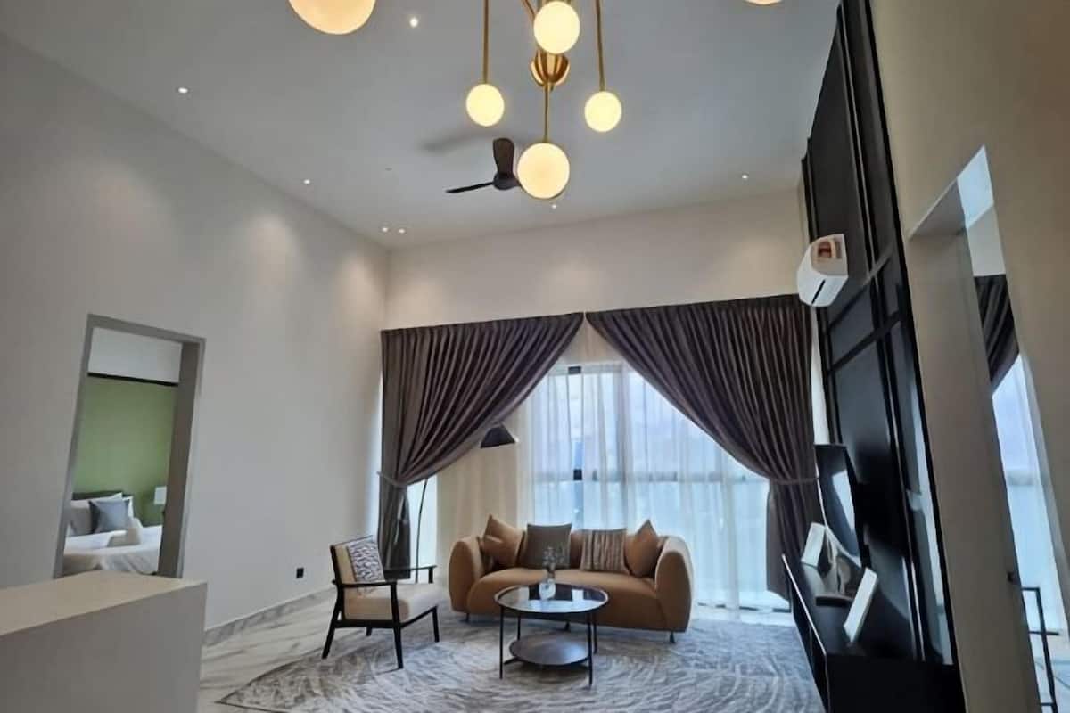 A modern hotel room with a sofa, armchair, coffee table, and large windows with curtains.