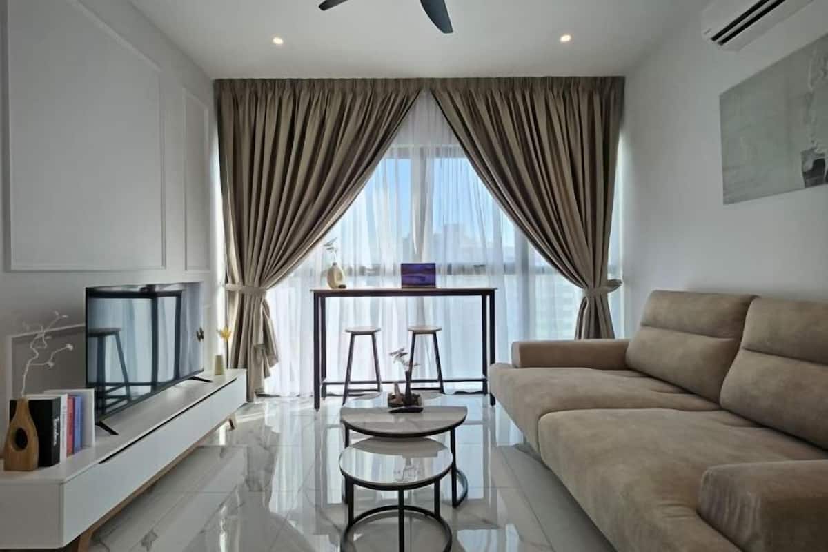 A modern living room with a flat-screen TV, a sofa, a coffee table, and a dining area with stools.