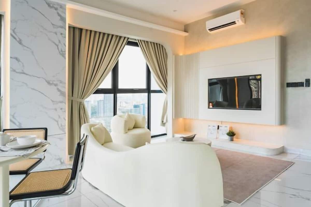 A modern hotel room with a bed, a TV, a dining area with a table and chairs, and a large window with curtains.