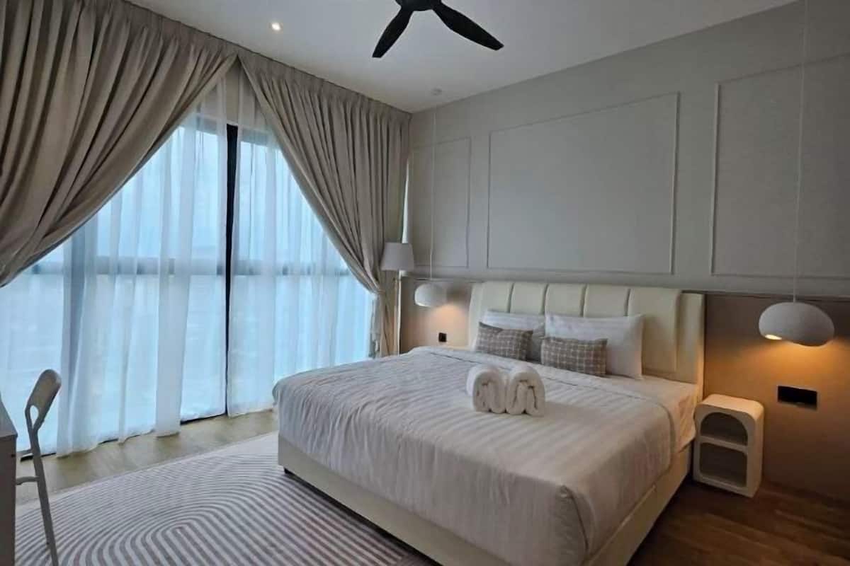 A hotel room with a large bed, a ceiling fan, a bedside table, and a view through the window.