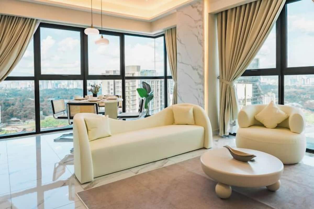 A modern living room with a sofa, armchair, and round coffee table. Large windows offer a city view.