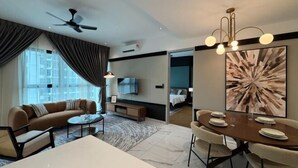 Une chambre d’hôtel moderne équipée d’un canapé, d’une table à manger, de chaises, d’un ventilateur de plafond, d’une télévision et d’un grand tableau abstrait.