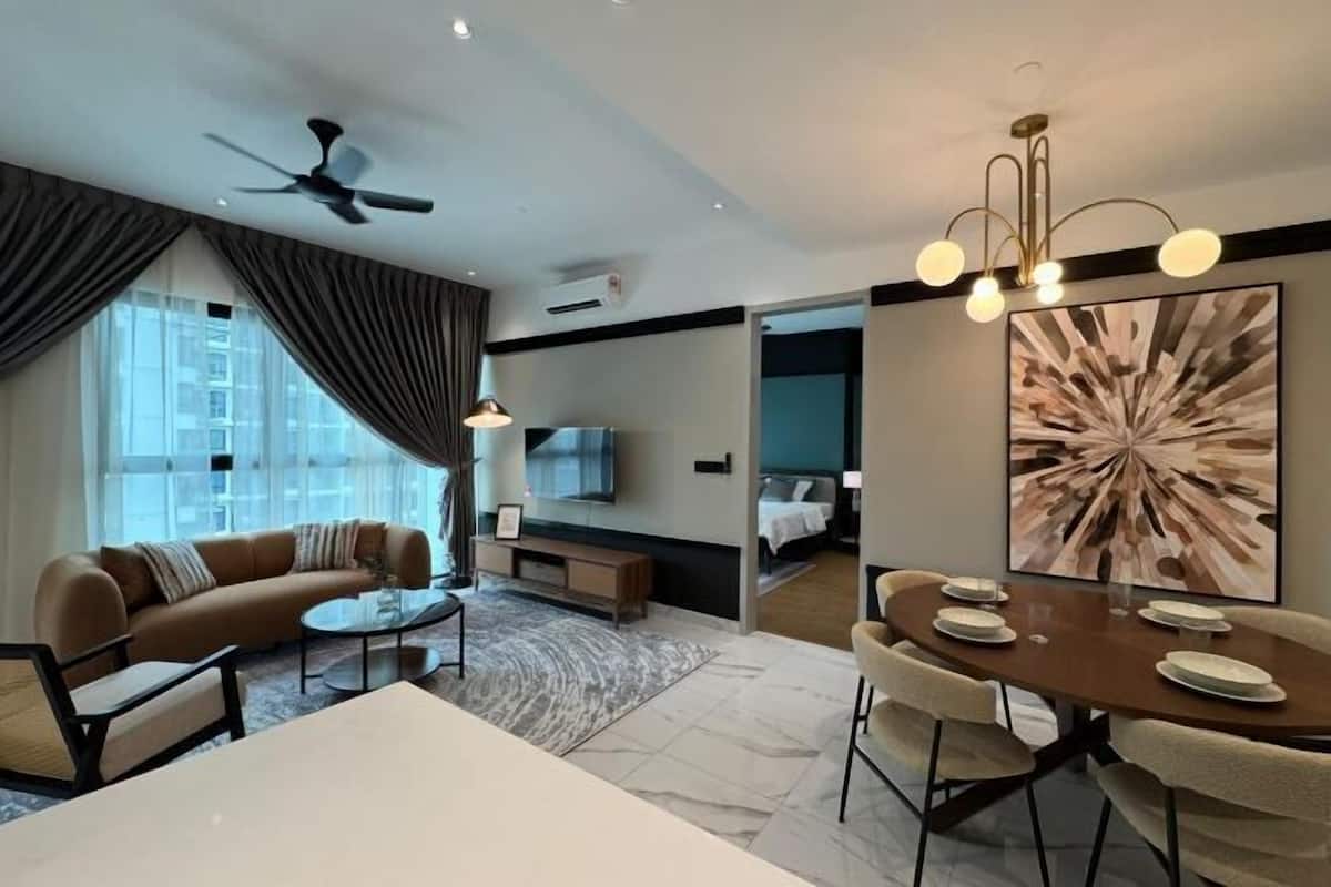 A modern hotel room with a sofa, dining table, chairs, a ceiling fan, a TV, and a large abstract painting.