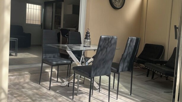 A patio area with a table and chairs, a clock on the wall, and a view of the interior.
